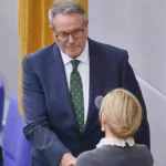 Alexander Schweitzer steht im Bundestag in dunklem Anzug und spricht mit einer Person im Vordergrund.