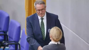 Alexander Schweitzer steht im Bundestag in dunklem Anzug und spricht mit einer Person im Vordergrund.