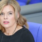 Julia Klöckner sitzt in einem hellen Saal auf einem blauen Stuhl und blickt zur Seite.