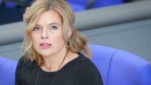 Julia Klöckner sitzt in einem hellen Saal auf einem blauen Stuhl und blickt zur Seite.