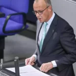 Friedrich Merz steht am Rednerpult im Deutschen Bundestag und blickt auf Unterlagen.
