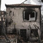 Ein durch Brand stark beschädigtes Wohnhaus mit verkohlter Fassade und zerstörten Fenstern zwischen verbrannten Bäumen.