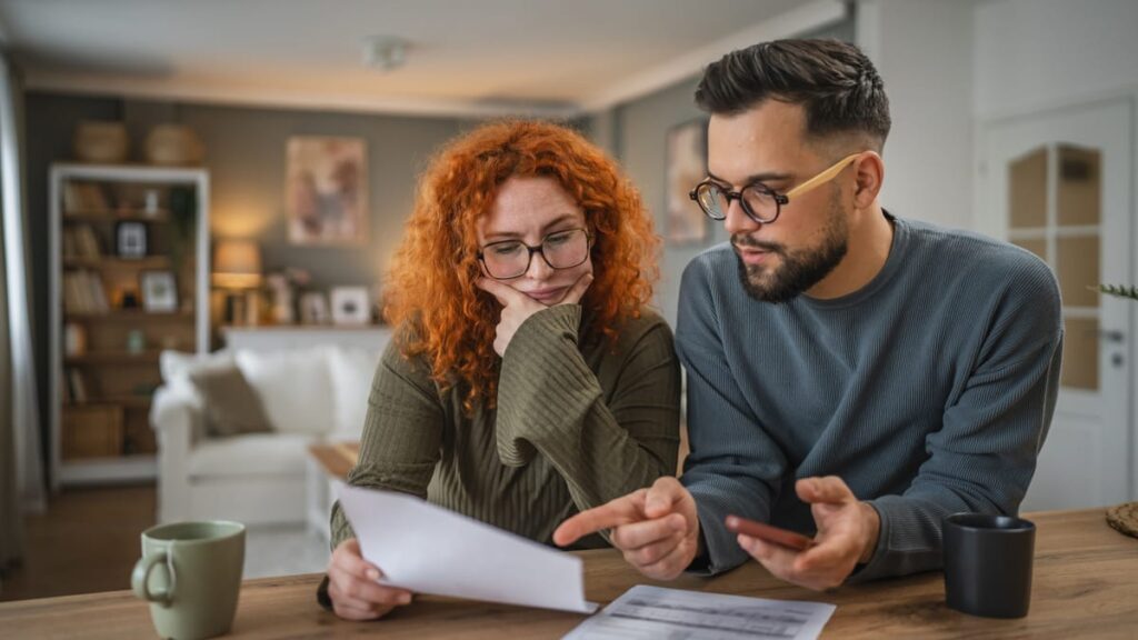 Ein Paar prüft gemeinsam Unterlagen am Tisch und bespricht Finanzen.