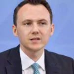 Pascal Reddig in dunklem Anzug vor blauem Hintergrund.
