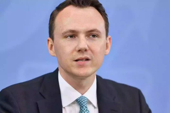 Pascal Reddig in dunklem Anzug vor blauem Hintergrund.