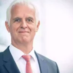 Porträt eines älteren Mannes im Anzug mit roter Krawatte vor hellem Hintergrund.