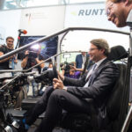 Andreas Scheuer sitzt in einem Fahrzeugrahmen und spricht mit Fotografen auf einer Messe.