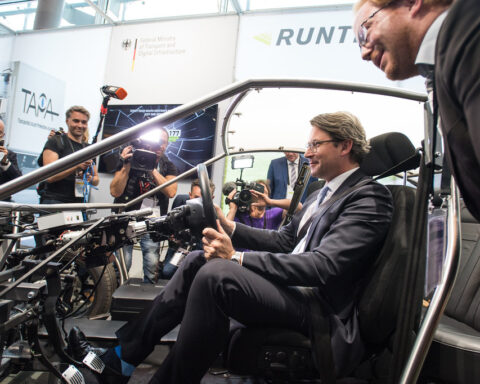 Andreas Scheuer sitzt in einem Fahrzeugrahmen und spricht mit Fotografen auf einer Messe.