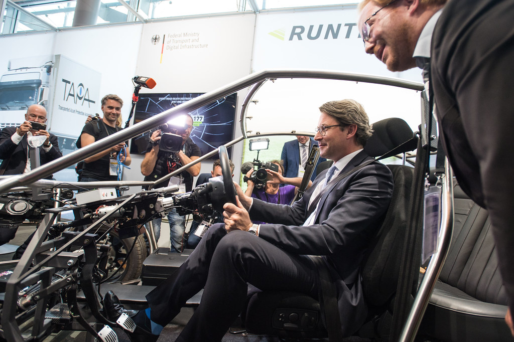 Andreas Scheuer sitzt in einem Fahrzeugrahmen und spricht mit Fotografen auf einer Messe.