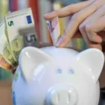 Hand steckt Euro-Banknoten in ein Sparschwein.