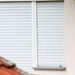 Geschlossenes Wohnungsfenster mit weißen Rollläden an einer Hausfassade.