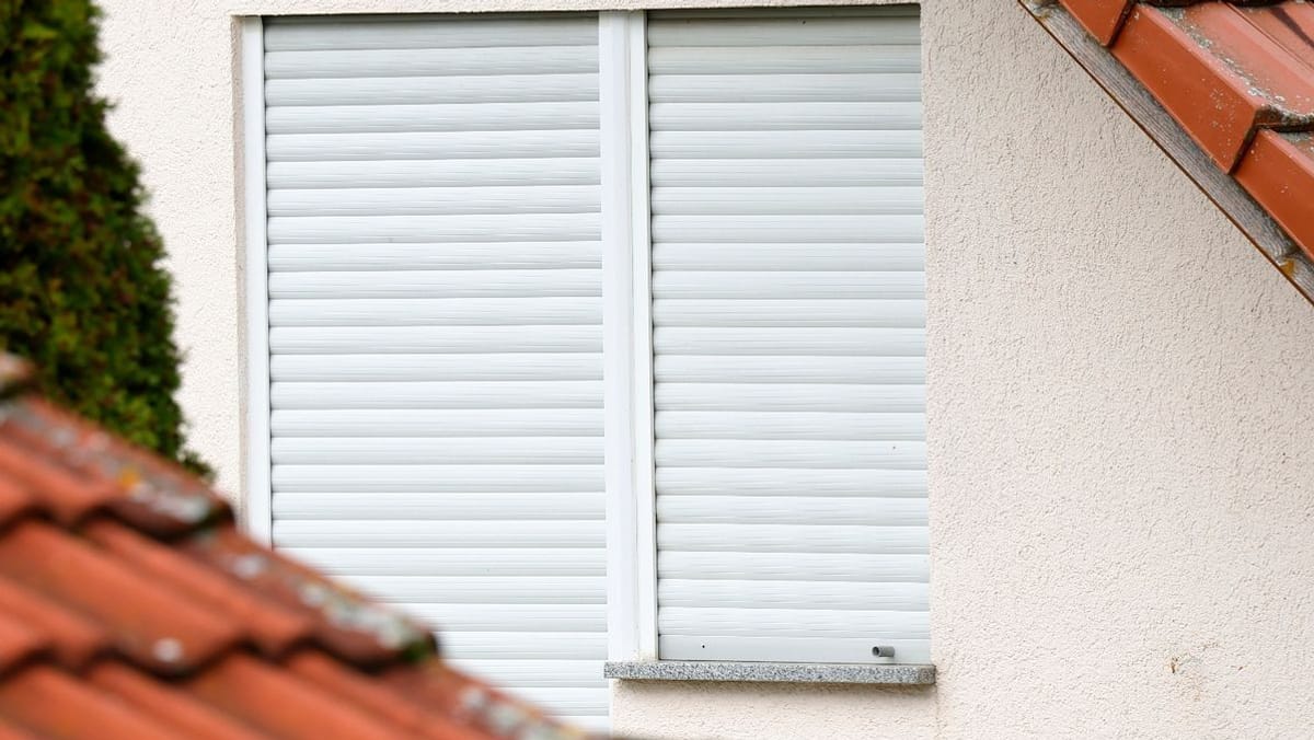 Geschlossenes Wohnungsfenster mit weißen Rollläden an einer Hausfassade.