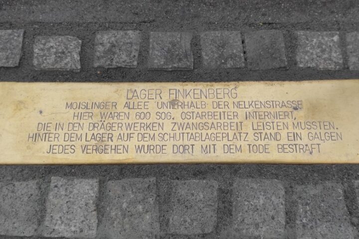 Gedenkplakette am Boden mit der Inschrift zum Lager Finkenberg und zum Zwangsarbeitseinsatz bei den Drägerwerken.