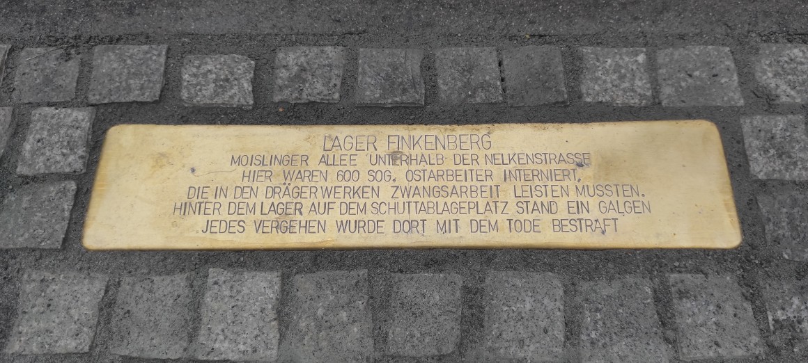 Drägerwerk meldet im dritten Quartal weniger Gewinn trotz Zollrückerstattungen 1 Gedenkplakette am Boden mit der Inschrift zum Lager Finkenberg und zum Zwangsarbeitseinsatz bei den Drägerwerken.