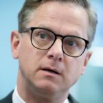 Carsten Linnemann in Nahaufnahme mit Brille vor blauem Hintergrund.