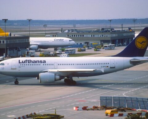 Lufthansa-Flugzeug auf dem Vorfeld am Flughafen, im Hintergrund weitere Maschinen und Abfertigungsfahrzeuge.