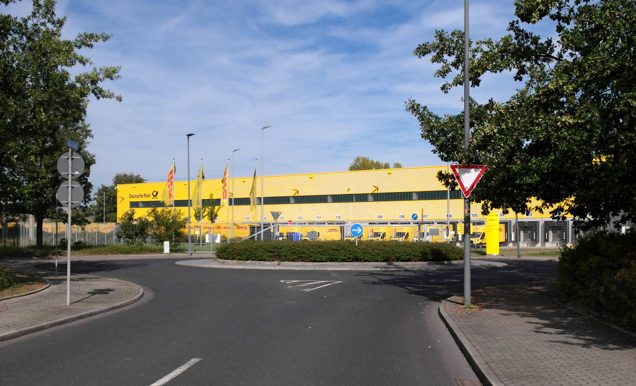 RBC startet DHL Group mit „Outperform“ und Kursziel von 67 Euro 1 Außenansicht eines gelben DHL-Depots der Deutschen Post mit Lieferfahrzeugen und Zufahrtsstraße.