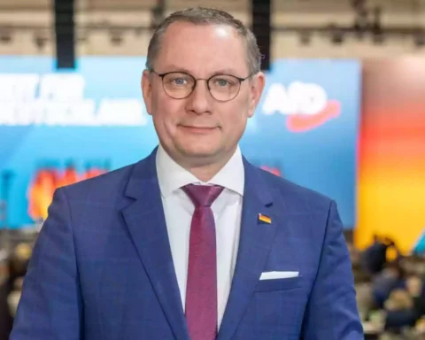 Tino Chrupalla steht in einem Veranstaltungsraum vor einem AfD-Hintergrund.