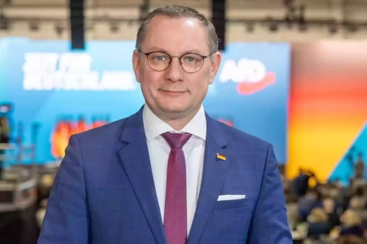 Tino Chrupalla steht in einem Veranstaltungsraum vor einem AfD-Hintergrund.