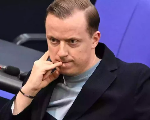 Ein Mann sitzt in einem Sitzungssaal des Bundestags und blickt nachdenklich nach vorn.