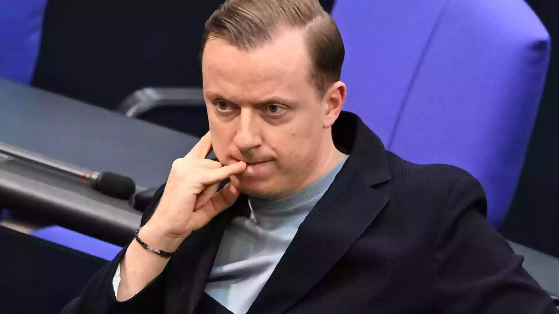 Ein Mann sitzt in einem Sitzungssaal des Bundestags und blickt nachdenklich nach vorn.