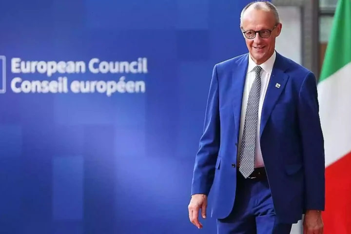 Friedrich Merz steht vor einer blauen European-Council-Wand neben einer EU-Flagge.