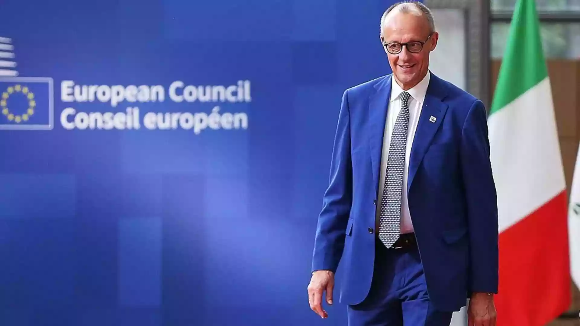 Merz verlangt Kürzungen beim EU-Finanzrahmen und erwartet kein Ergebnis 1 Friedrich Merz steht vor einer blauen European-Council-Wand neben einer EU-Flagge.