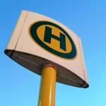 Nahaufnahme eines gelb-schwarzen Haltestellenschilds vor blauem Himmel.
