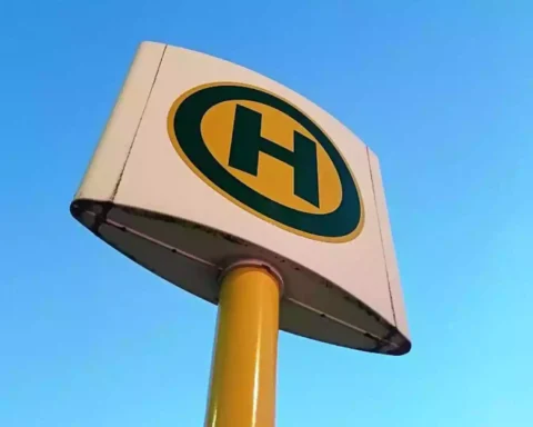 Nahaufnahme eines gelb-schwarzen Haltestellenschilds vor blauem Himmel.