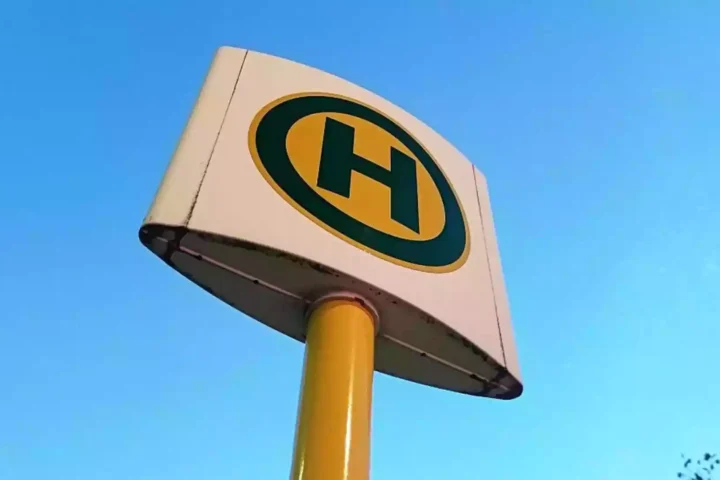 Nahaufnahme eines gelb-schwarzen Haltestellenschilds vor blauem Himmel.