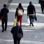 Menschen gehen auf einem gepflasterten Gehweg durch eine Fußgängerzone.