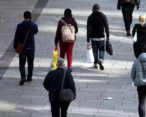 Menschen gehen auf einem gepflasterten Gehweg durch eine Fußgängerzone.