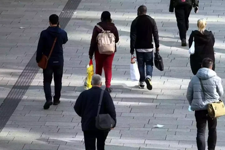 Menschen gehen auf einem gepflasterten Gehweg durch eine Fußgängerzone.