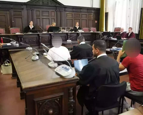 Blick in einen Gerichtssaal mit Richtern, Verteidigern und Angeklagten während einer Verhandlung.