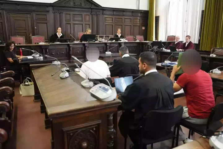 Blick in einen Gerichtssaal mit Richtern, Verteidigern und Angeklagten während einer Verhandlung.