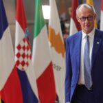 Friedrich Merz steht vor mehreren EU-Flaggen bei einem Treffen.