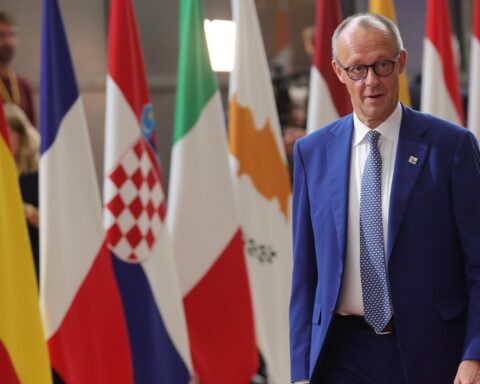Friedrich Merz steht vor mehreren EU-Flaggen bei einem Treffen.