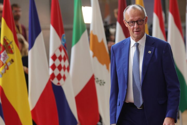 Friedrich Merz steht vor mehreren EU-Flaggen bei einem Treffen.