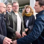 Mehrere Politiker stehen vor einem Gebäude und sprechen miteinander auf dem Gehweg.