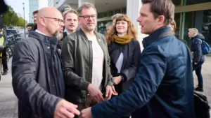 Mehrere Politiker stehen vor einem Gebäude und sprechen miteinander auf dem Gehweg.