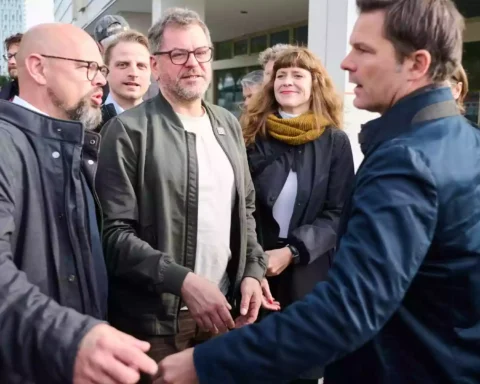 Mehrere Politiker stehen vor einem Gebäude und sprechen miteinander auf dem Gehweg.
