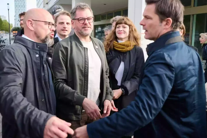 Mehrere Politiker stehen vor einem Gebäude und sprechen miteinander auf dem Gehweg.