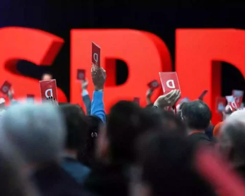 Menschen halten auf einem SPD-Parteitag rote Abstimmungskarten vor großen roten SPD-Buchstaben.