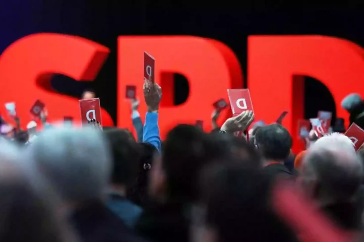 Menschen halten auf einem SPD-Parteitag rote Abstimmungskarten vor großen roten SPD-Buchstaben.