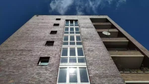 Blick von unten auf die Fassade eines Wohnhauses mit Balkonen und blauem Himmel.