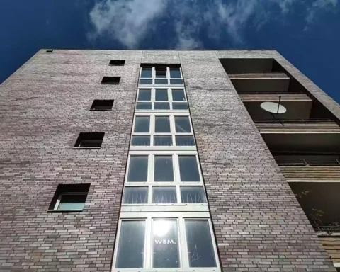 Blick von unten auf die Fassade eines Wohnhauses mit Balkonen und blauem Himmel.