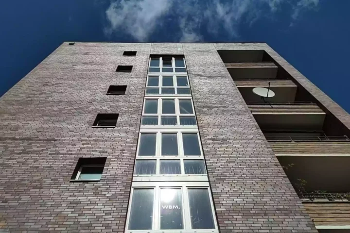 Blick von unten auf die Fassade eines Wohnhauses mit Balkonen und blauem Himmel.