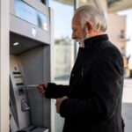 Älterer Mann hebt am Geldautomaten Geld ab.