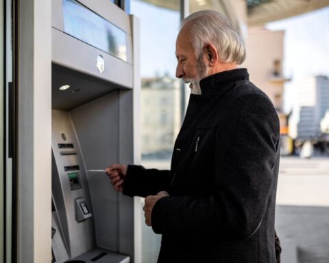 Älterer Mann hebt am Geldautomaten Geld ab.