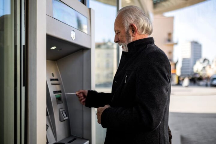 Älterer Mann hebt am Geldautomaten Geld ab.